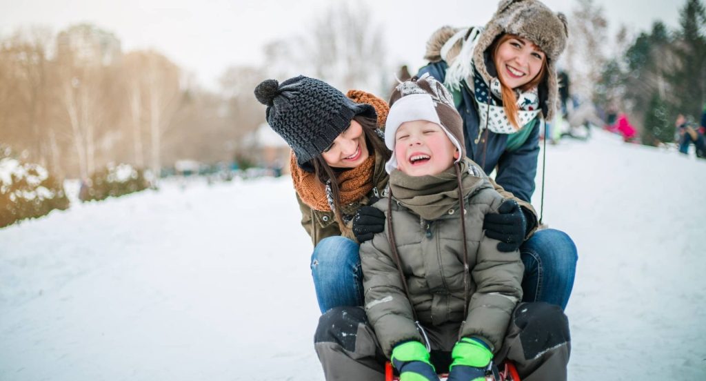 Deux femmes et un enfant s'amusent à glisser dans la neige.